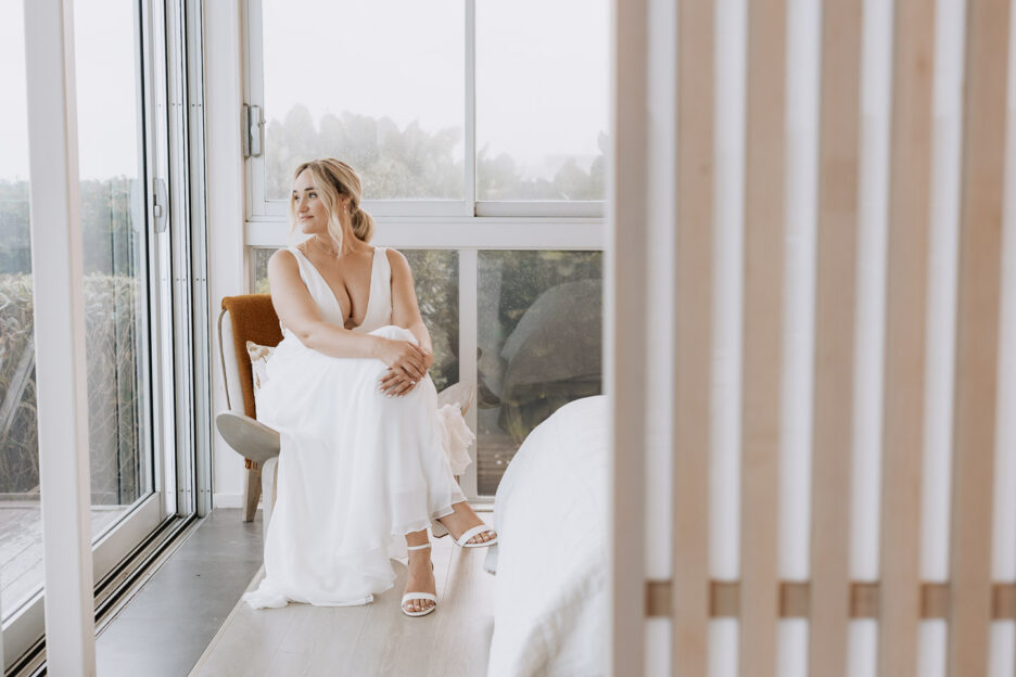 bride sitting in corner of beach house looking out to sea