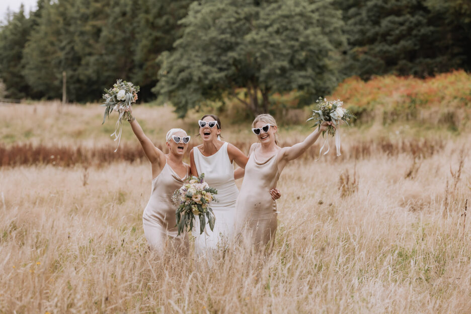 in golden field of high grass bride celebrates with bridesmaids in beige dresses