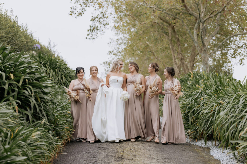 Bride with bridesmaids in smokey pink dresses walk on driveway Eagle ridge wedding venue