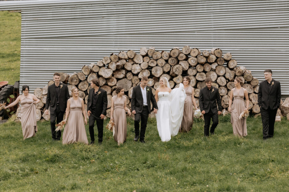 wedding party in pink and black walk by firewood barn eagle Ridge in field