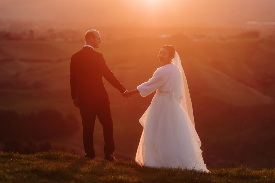 beautiful wedding photo bride and groom walking into the sunset at golden light in Tauranga hills