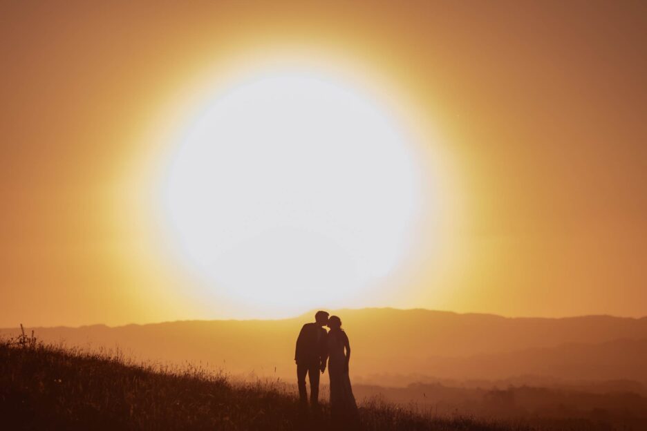 bride and groom kiss silhouetted by sun